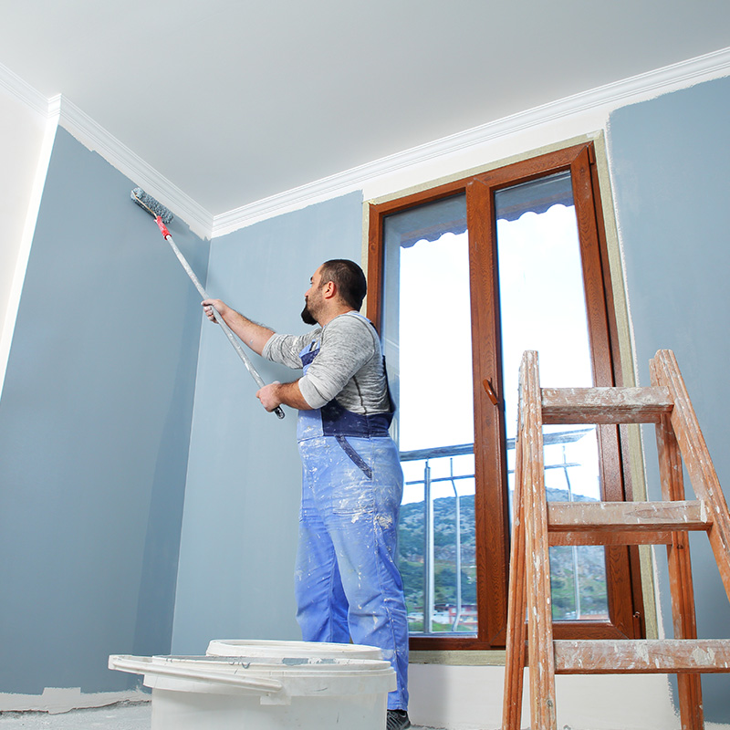 Painter man at work takes the color with paint roller from the bucket